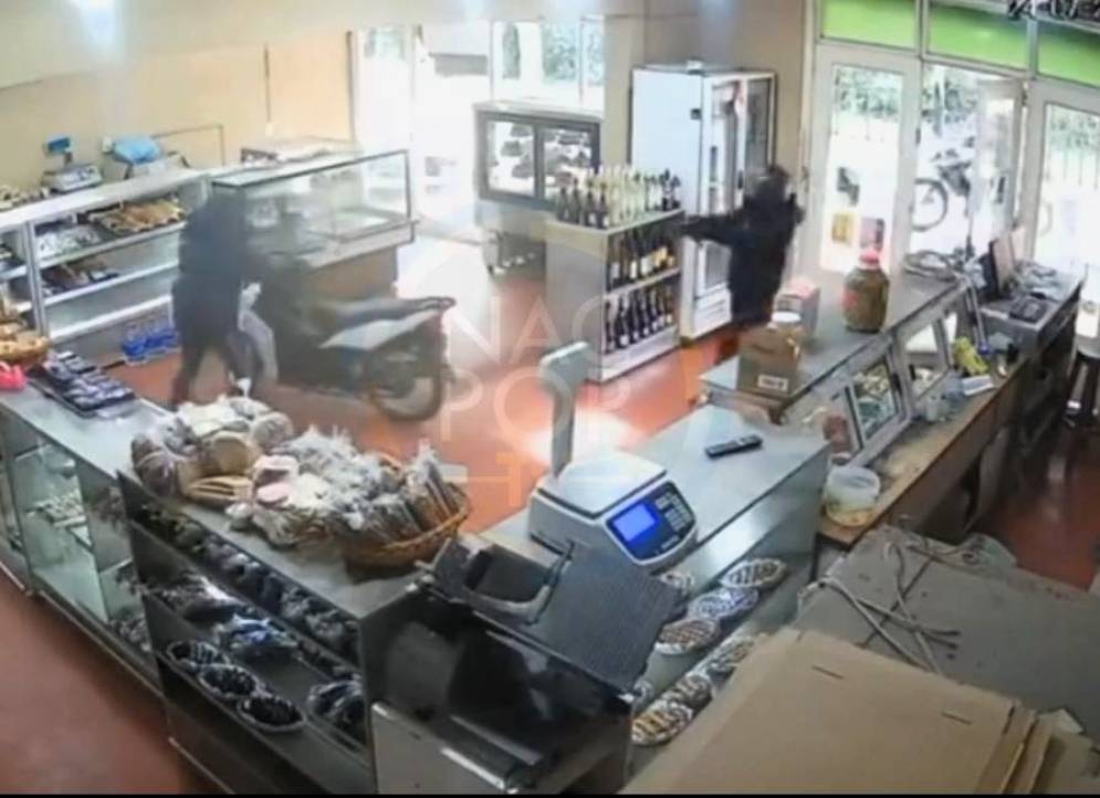 El ladrón, con casco, apuntando a la víctima, dentro de la panadería.